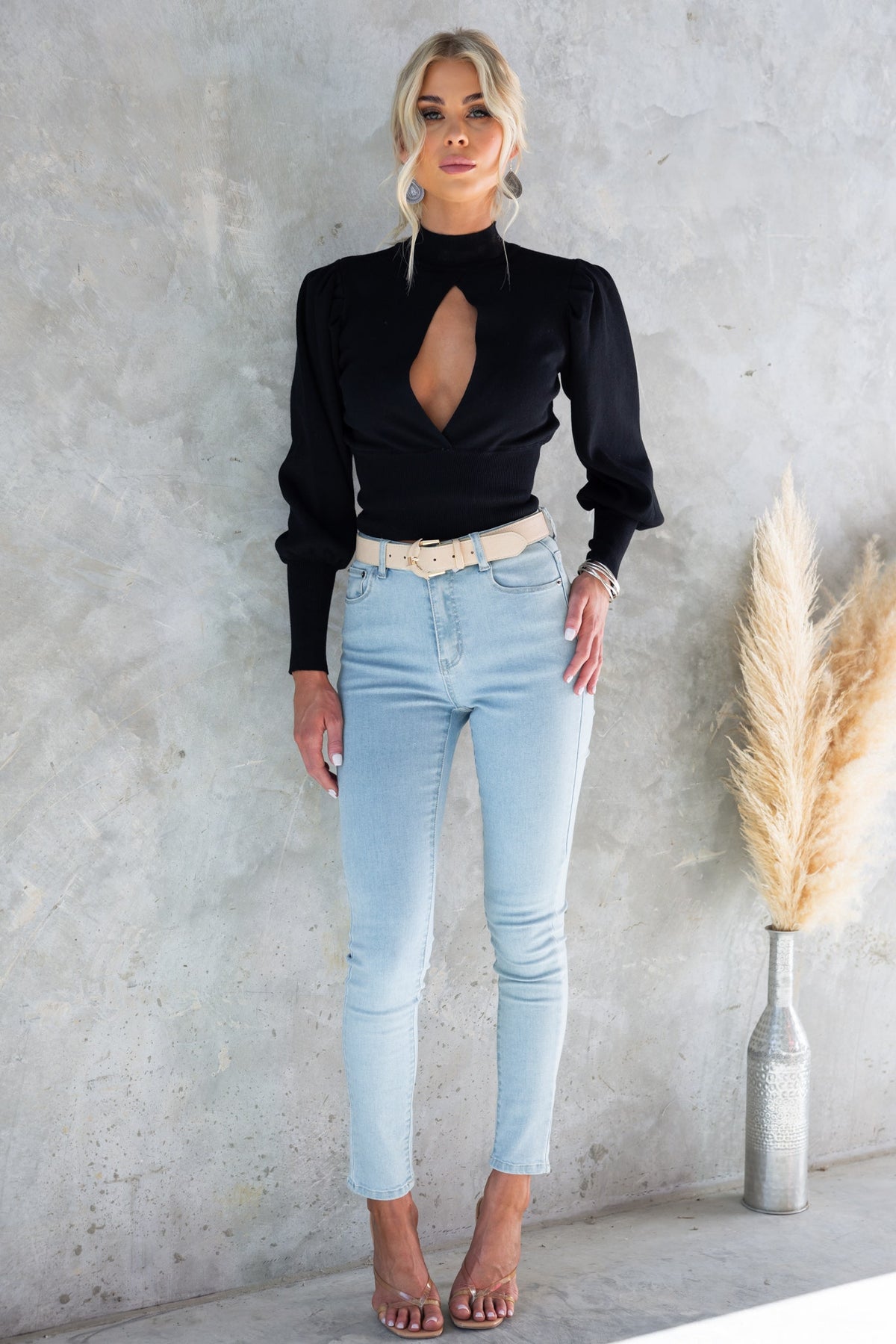Model wearing a stylish black Sania Top with a high neckline and cut-out detail, paired with light blue jeans.