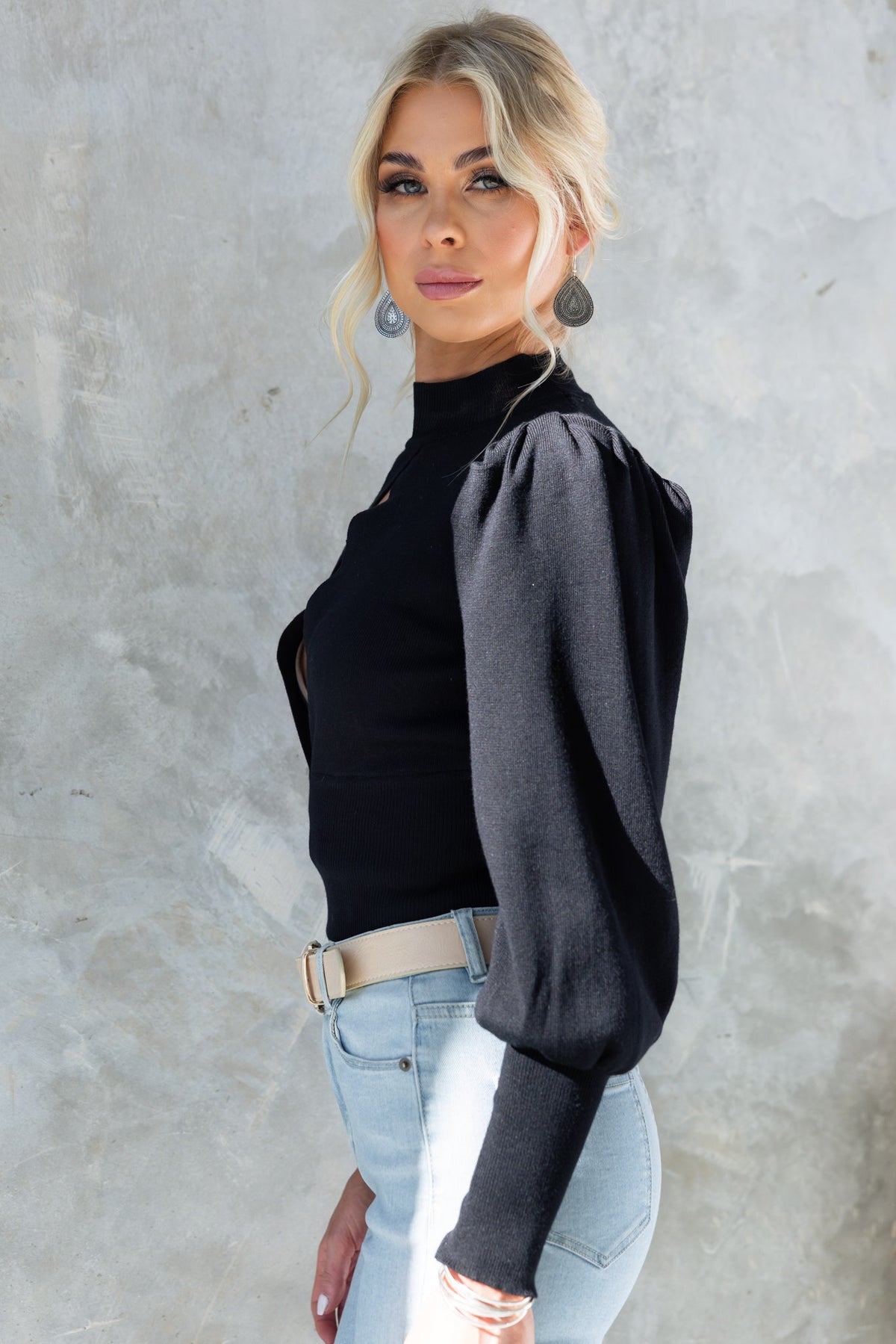Model wearing a black Sania Top with high neckline and puff sleeves, paired with light jeans.