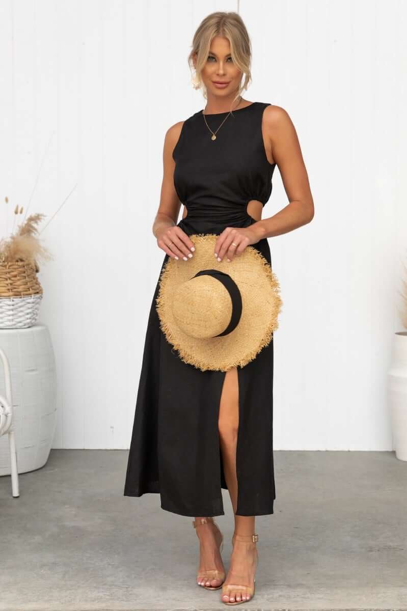 Rozita Midi Dress in black linen blend with cut-out sides and front slit, styled with a straw hat for summer fashion.