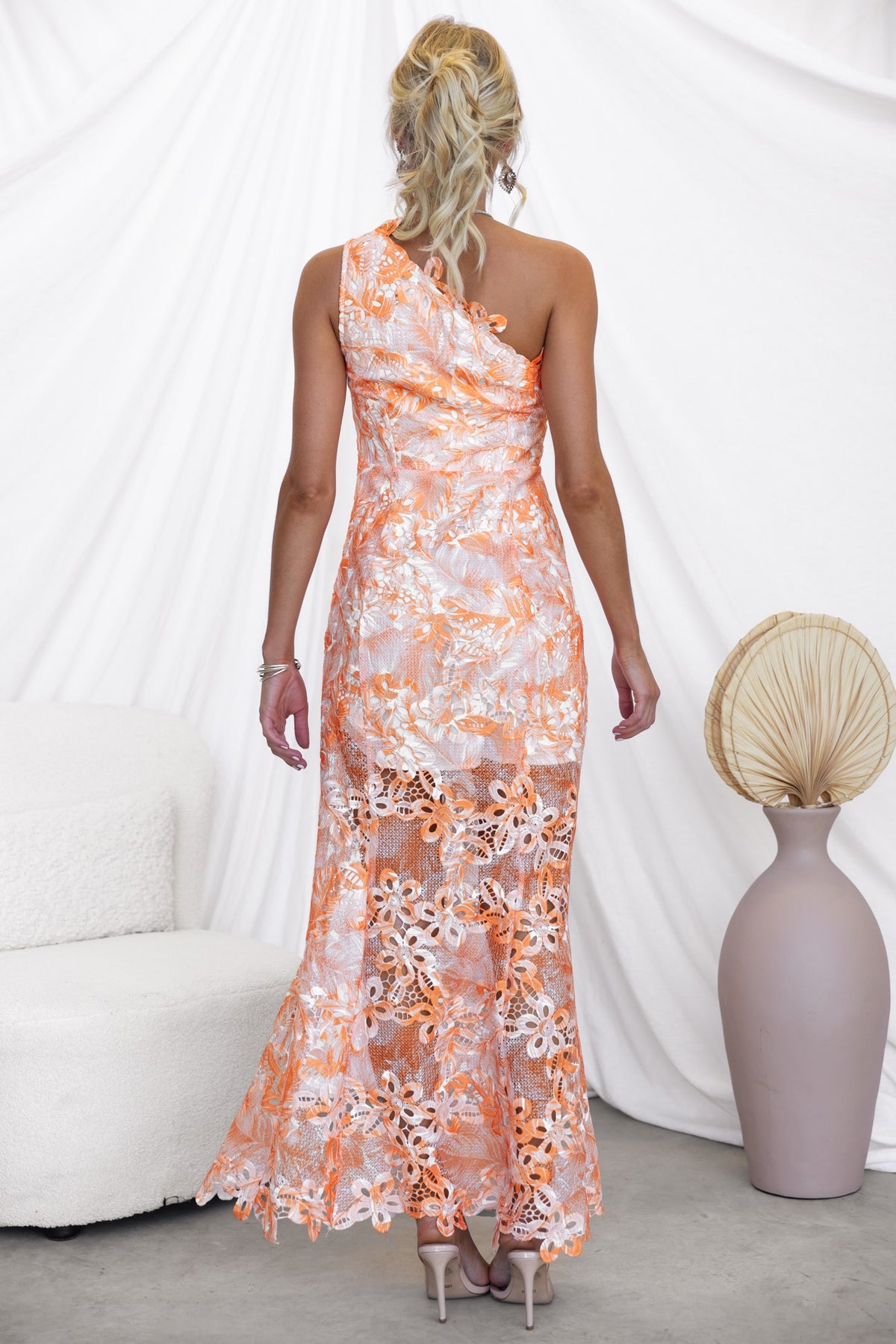 Back view of Racha Maxi Dress featuring one-shoulder design, floral lace details, and a flowing silhouette in orange.