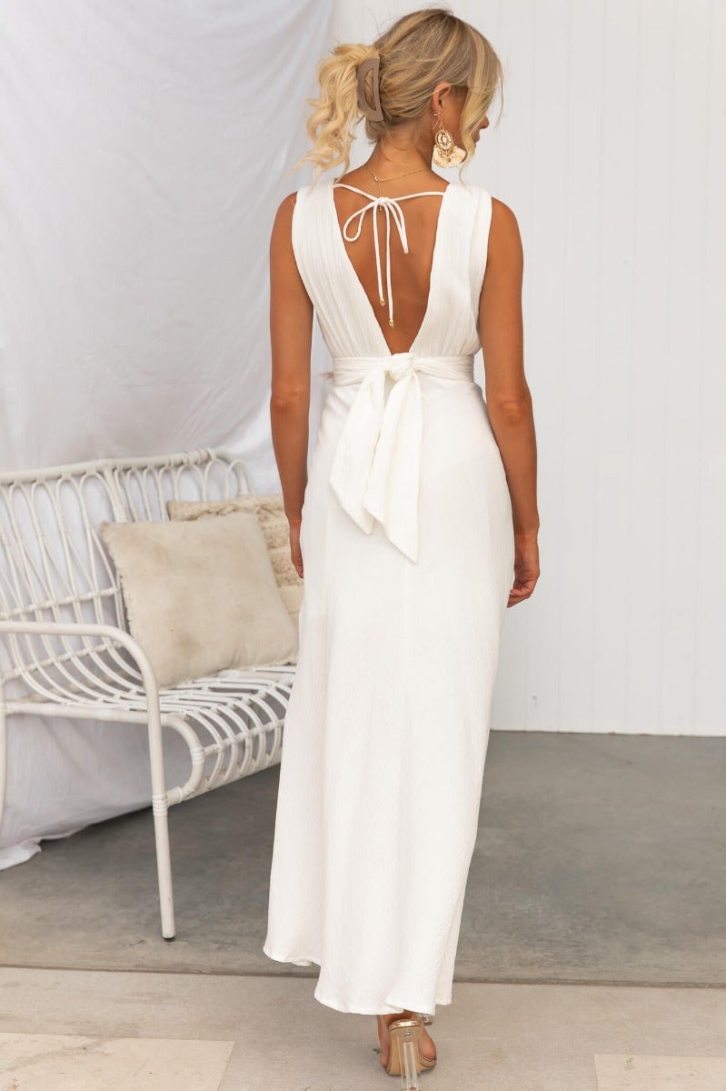 Back view of a model in the Gia Maxi Dress featuring a tie detail and open back design in textured white fabric.