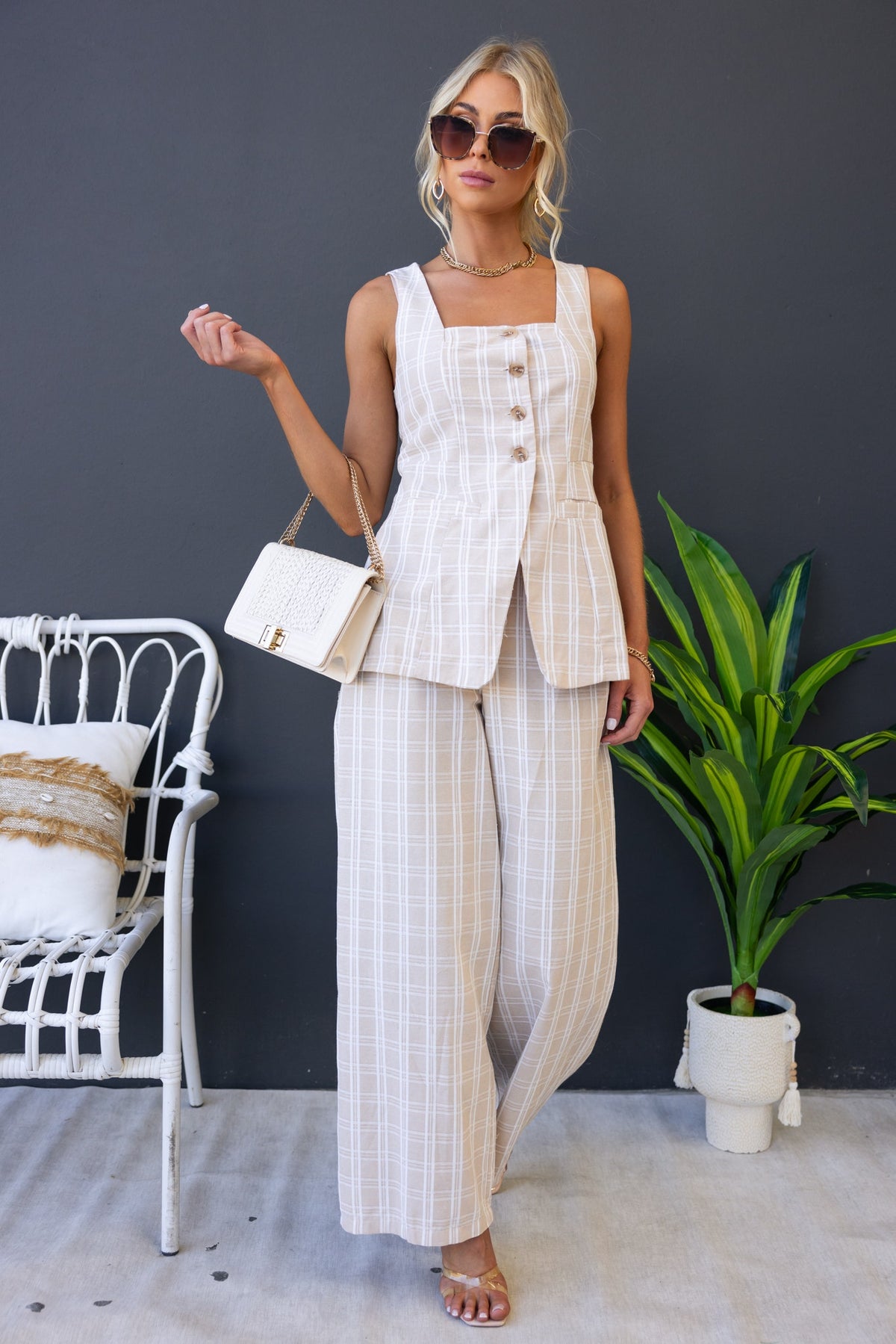 Stylish woman in beige Bexley Pants and matching top, accessorized with sunglasses and a handbag, posing indoors.