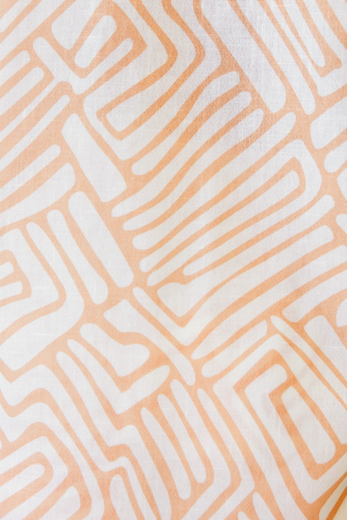 Close-up of abstract patterned fabric in soft orange and white shades, ideal for stylish apparel like the Tari Shirt.