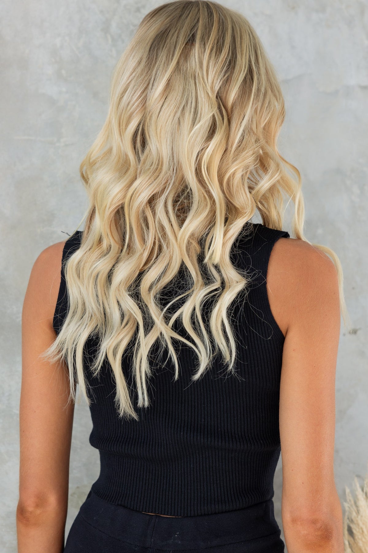 Back view of a model wearing a black ribbed knit top with long wavy blonde hair.