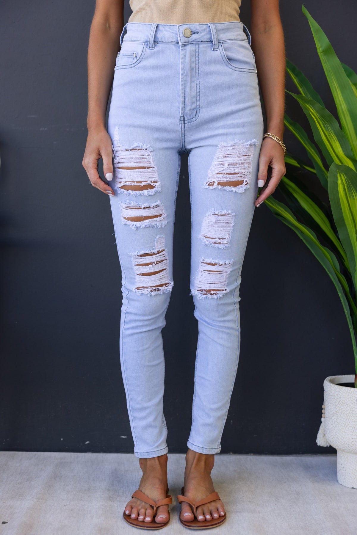 Milos Jeans in light blue with distressed rips, high-waisted fit, styled with casual sandals against a dark background.