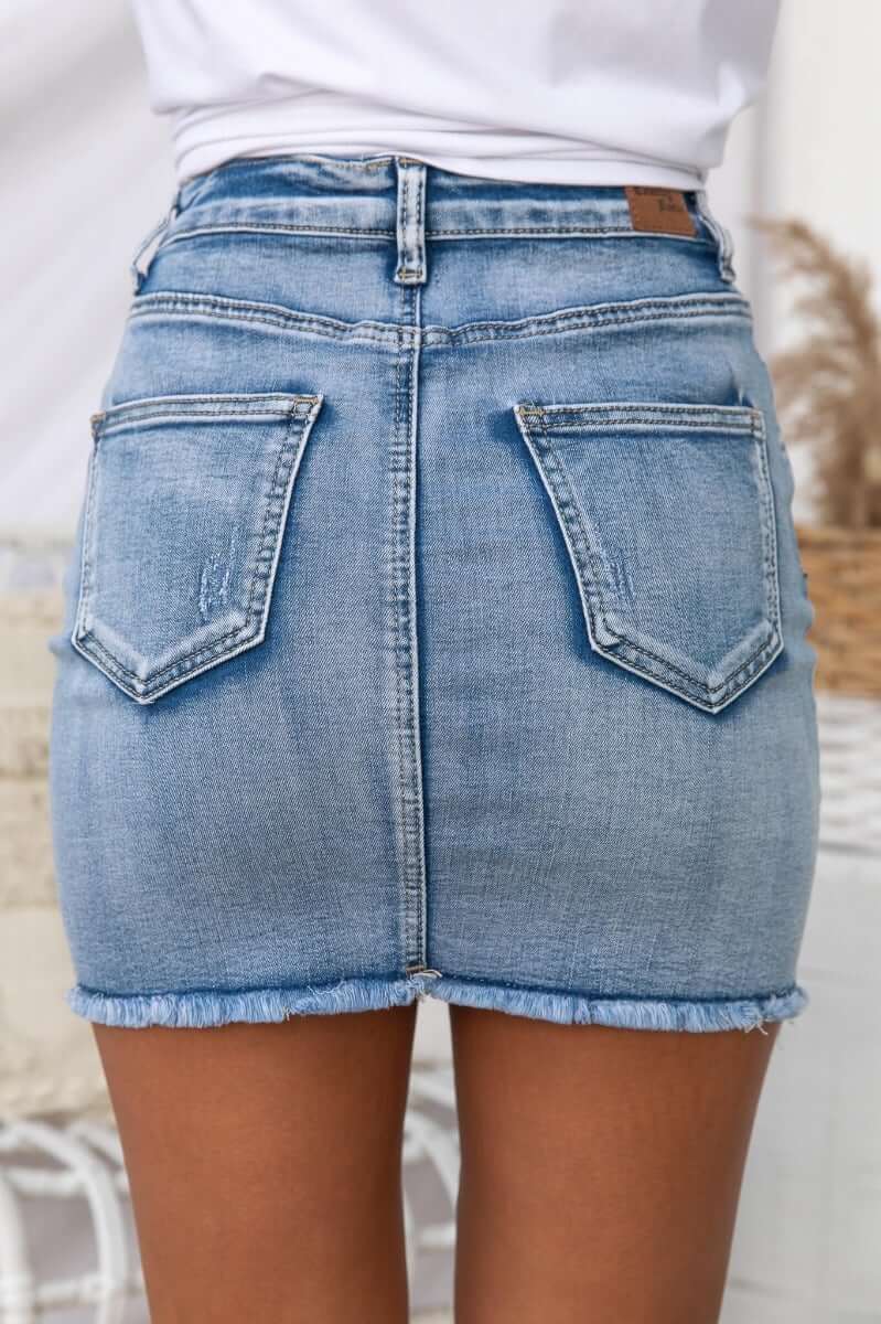 Back view of Nice For What Skirt, featuring distressed pockets and raw hemline in light blue denim.