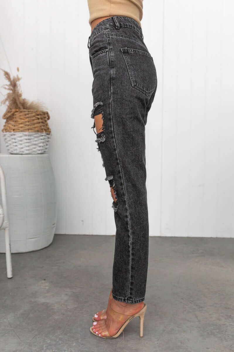 Side view of black wash distressed mom jeans with high waist fit and rips, styled with heels.