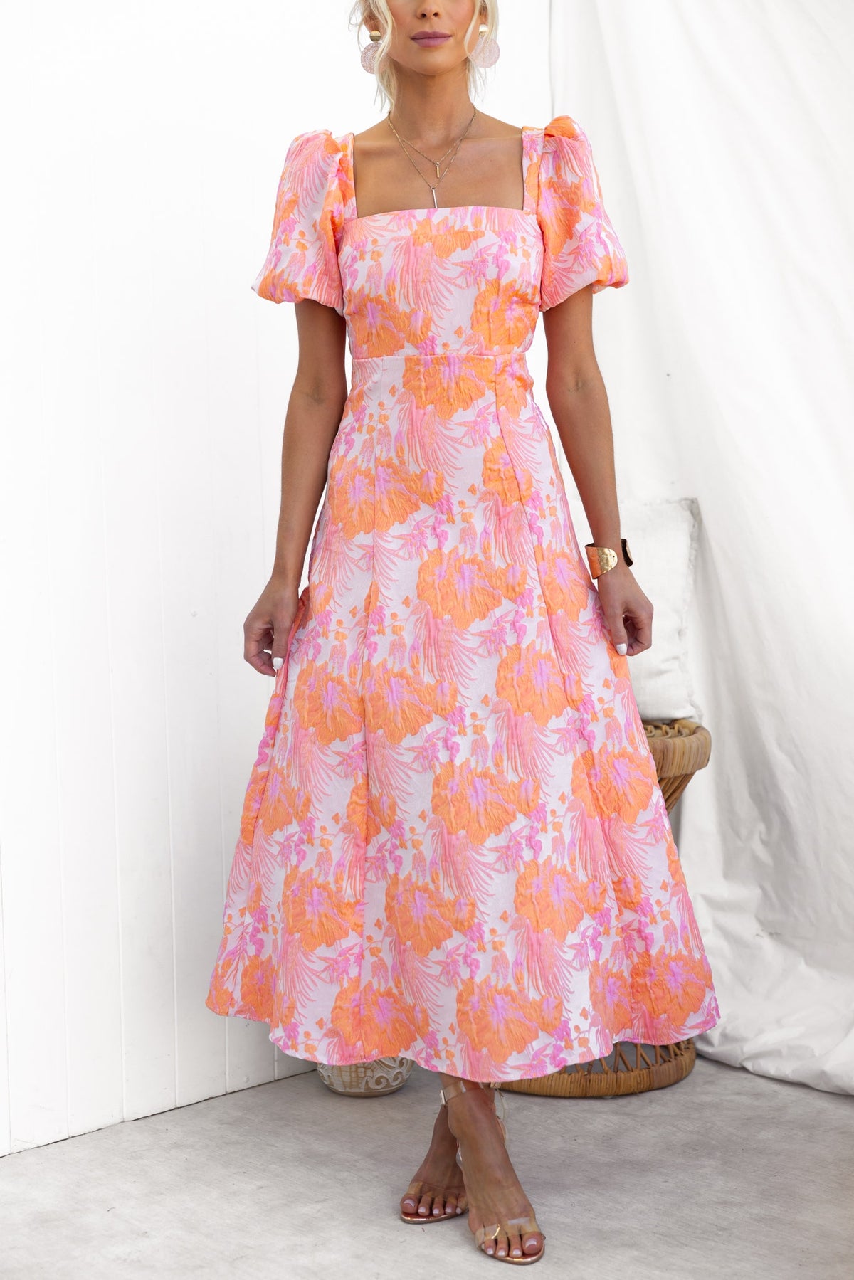 Sachin Maxi Dress features a square neckline, puff sleeves, and a vibrant floral pattern in pink and orange.