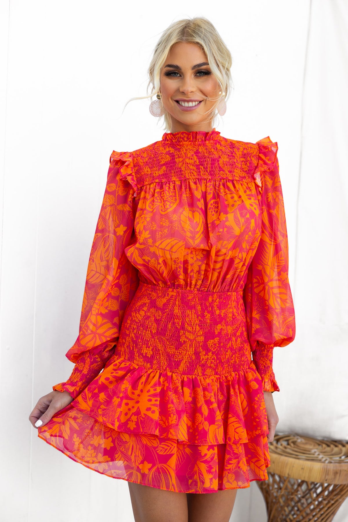 Model wearing Ginevra Dress in vibrant pink and orange chiffon, featuring ruffled neckline and elastic waistband.