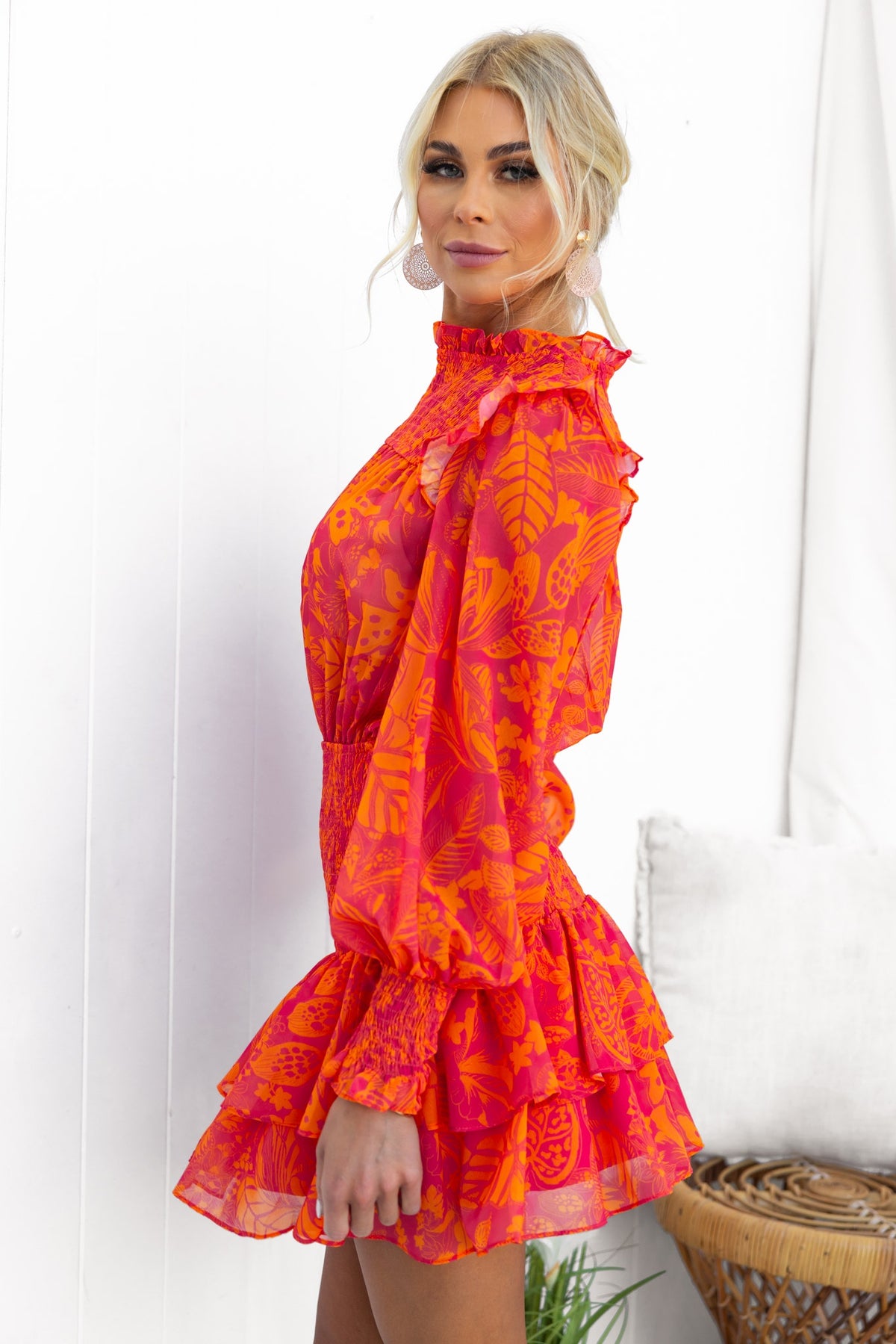 Model wearing the Ginevra Dress, showcasing vibrant orange chiffon with floral patterns, puff sleeves, and a ruffled hem.