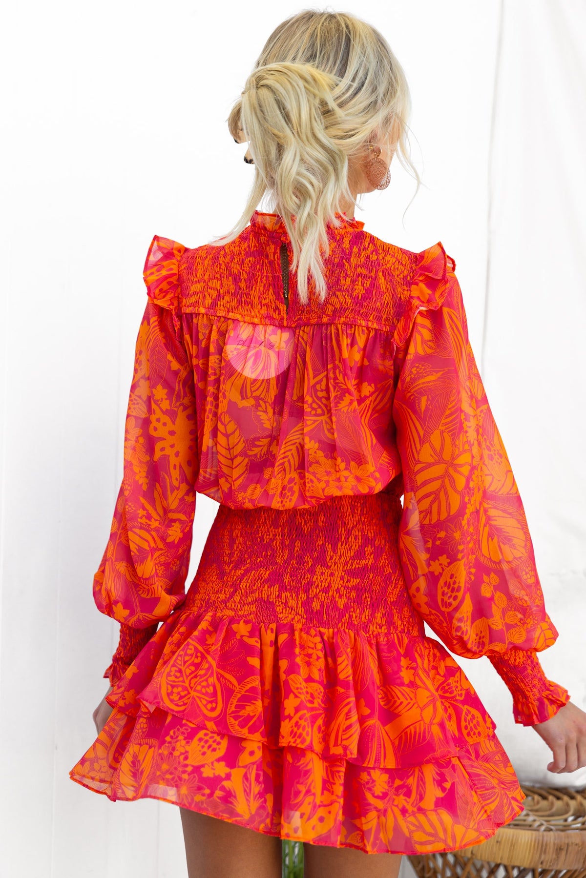 Back view of a vibrant pink and orange floral chiffon Ginevra Dress with ruffled sleeves and a fitted skirt.