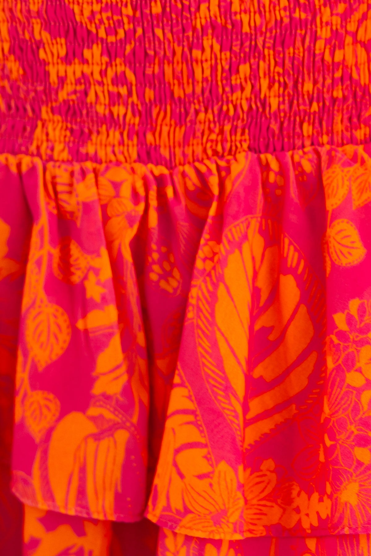 Close-up of colorful Ginevra Dress featuring floral patterns in pink and orange with ruffle detail.