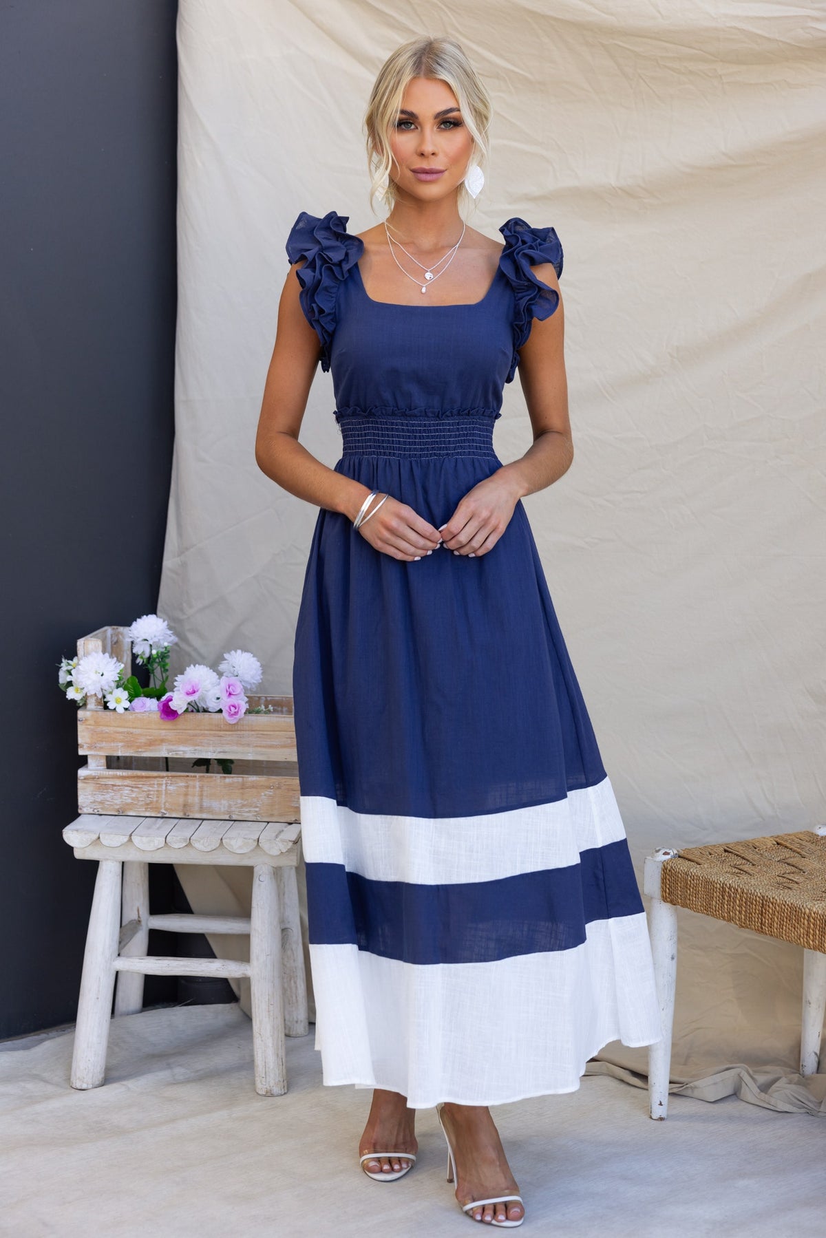 Woman in a navy Kape Maxi Dress with ruffled sleeves and a white striped hem, styled for a chic summer look.