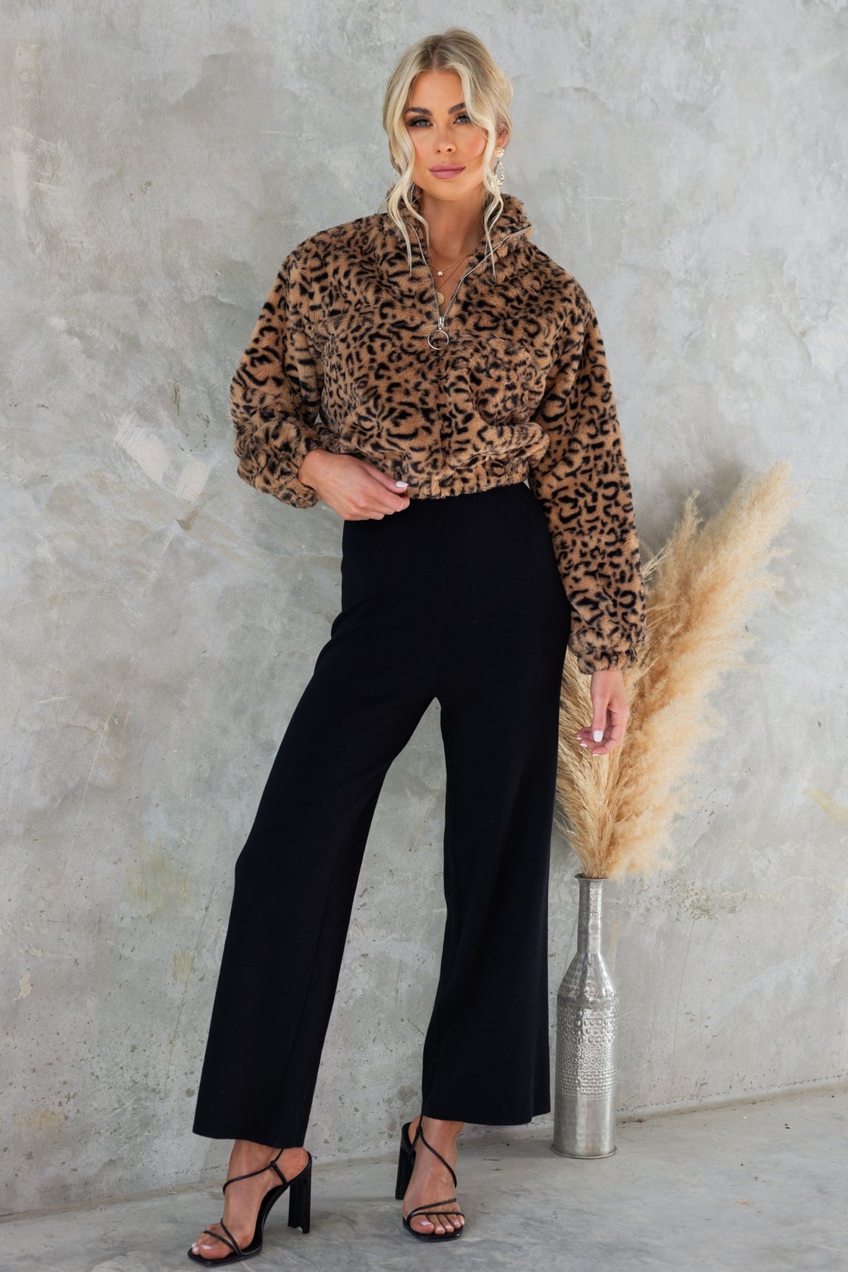 Model wearing a cropped leopard print jumper with half-zip, styled with black wide-leg pants against a textured background.