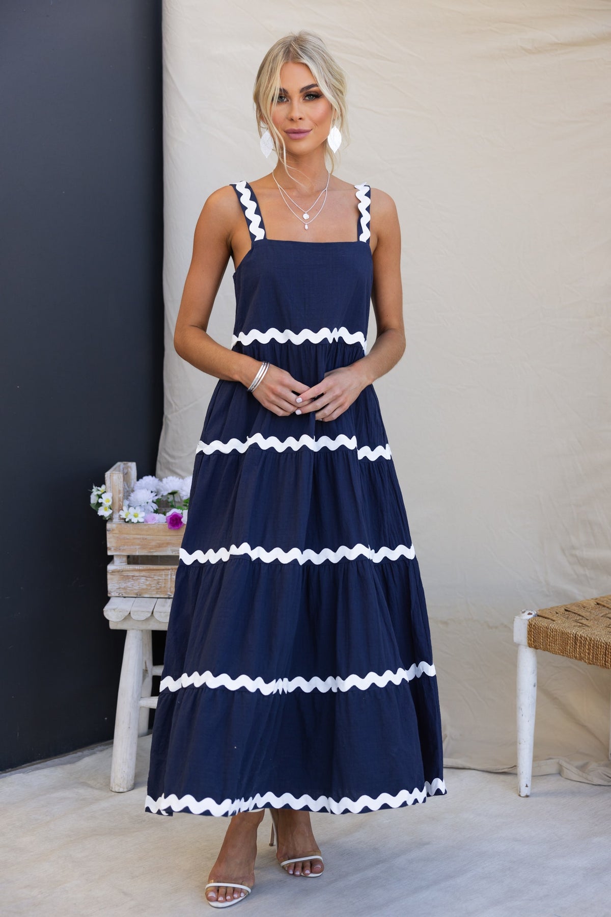 Navy Nori maxi dress featuring a square neckline, ruffled trim, and a relaxed fit, styled with delicate jewelry.