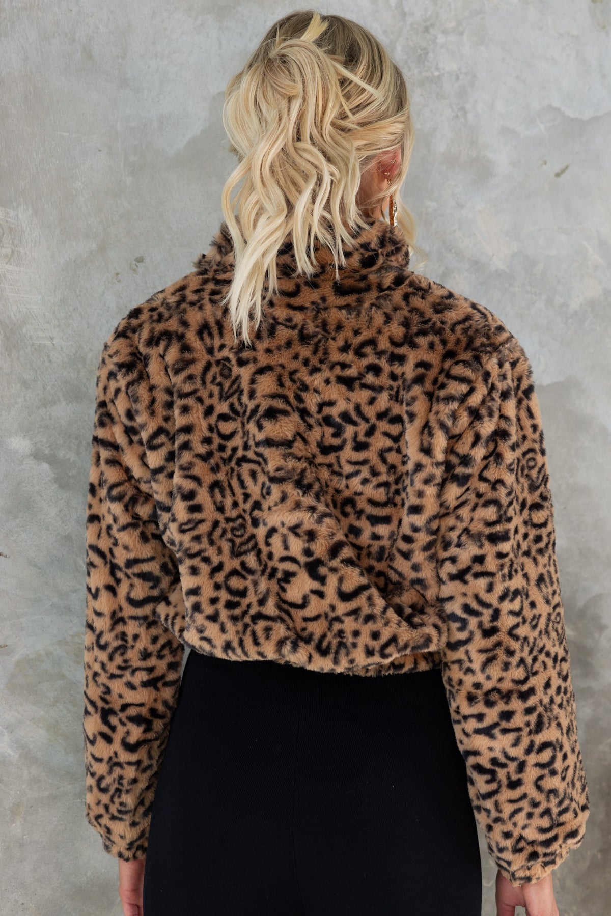 Back view of a woman in a leopard print half-zip jumper, featuring cozy fabric and a stylish cropped fit.