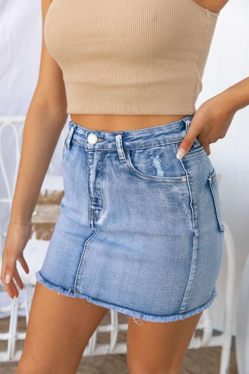 Model wearing Nice For What Skirt featuring distressed details, raw hemline, and pockets in light blue denim.