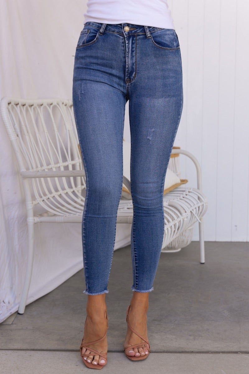 Model wearing Juicebox Jeans with mid waist fit, distressed details, and raw hem in blue wash.