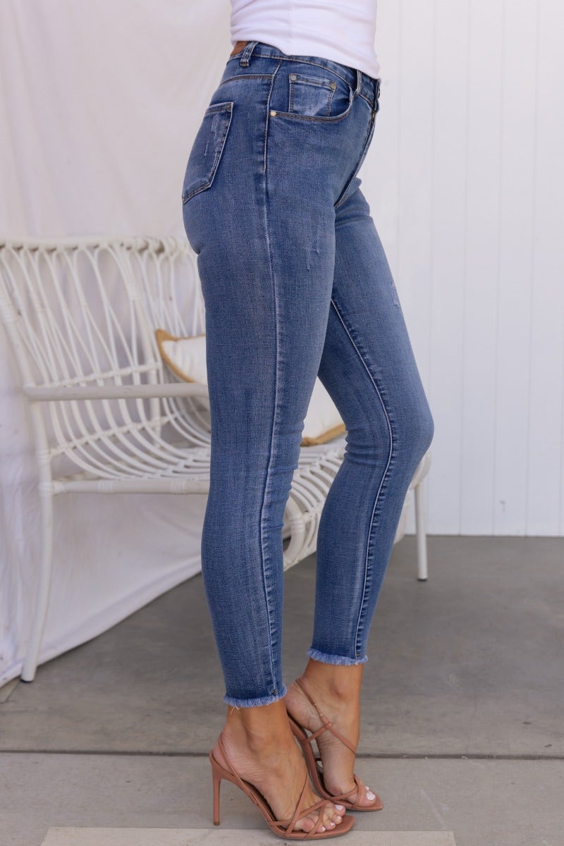 Side view of Juicebox Jeans, mid waist fit with distressed details and raw hem, showcasing a standard skinny fit.