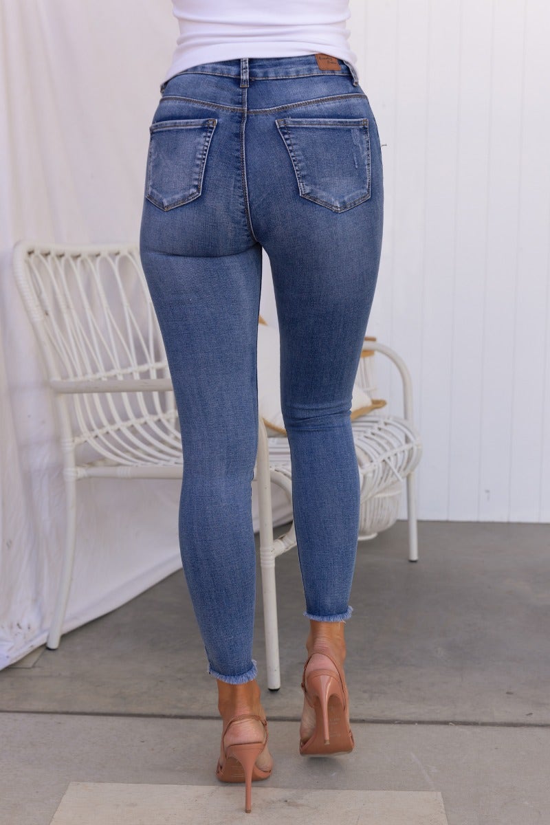 Juicebox Jeans featuring mid waist fit, distressed details, raw hem, and a standard skinny fit, worn with stylish heels.