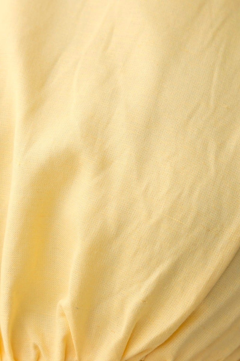 Close-up of a textured yellow linen fabric, highlighting its softness and natural fibers for a maxi dress.