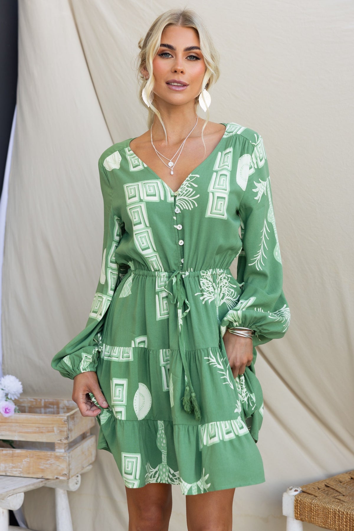 Model wearing Gratias Dress in green, featuring V-neckline, button-up front, elastic waistband, and pockets.