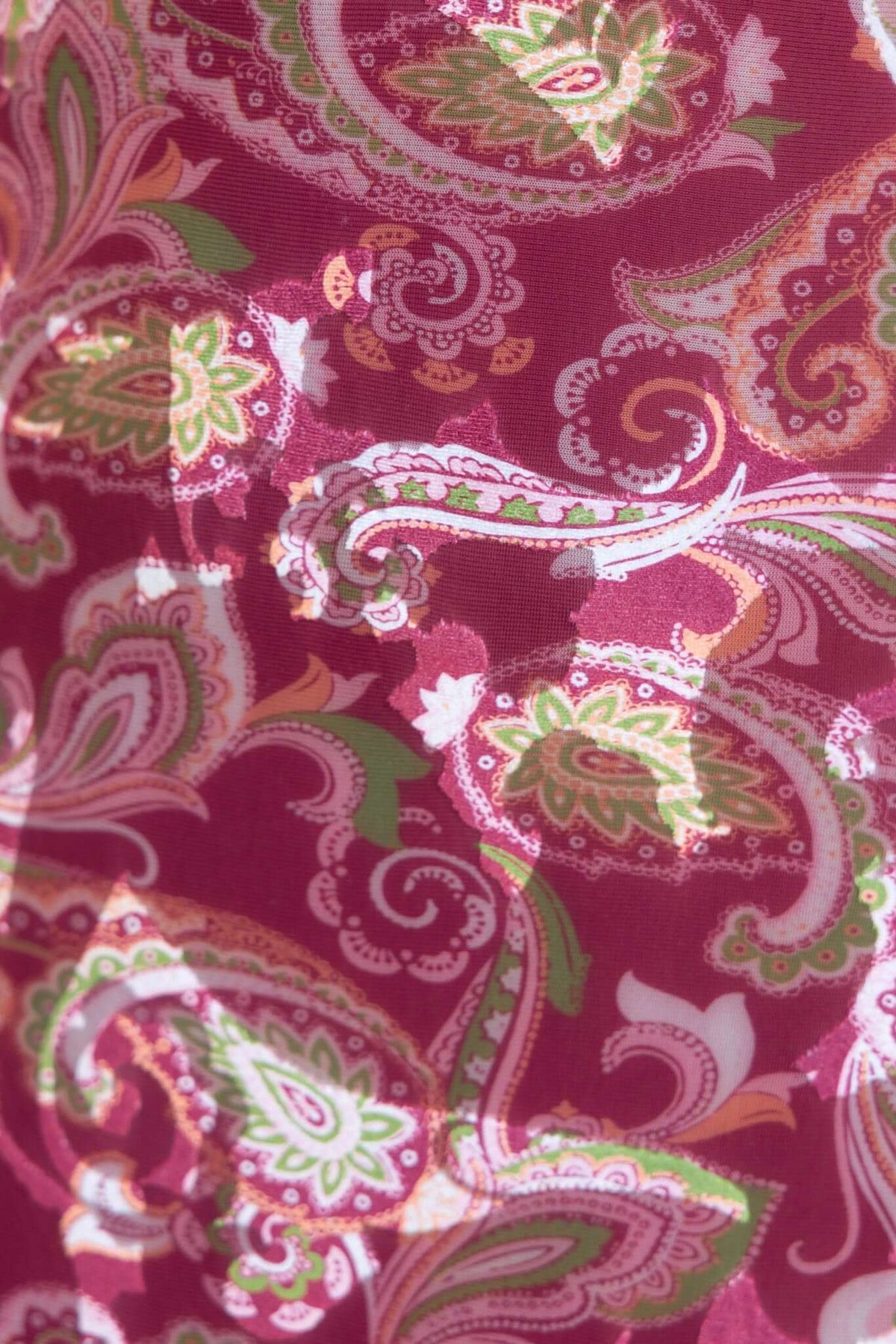 Close-up of a pink paisley fabric with green and white floral patterns, featuring texture and vibrant colors.