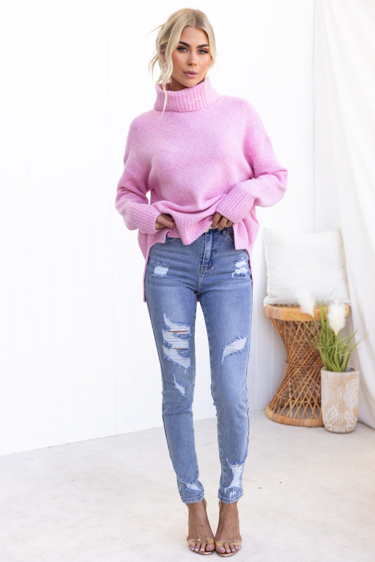 Model wearing a pink Orion Jumper with turtle neckline, paired with distressed blue jeans in a bright setting.
