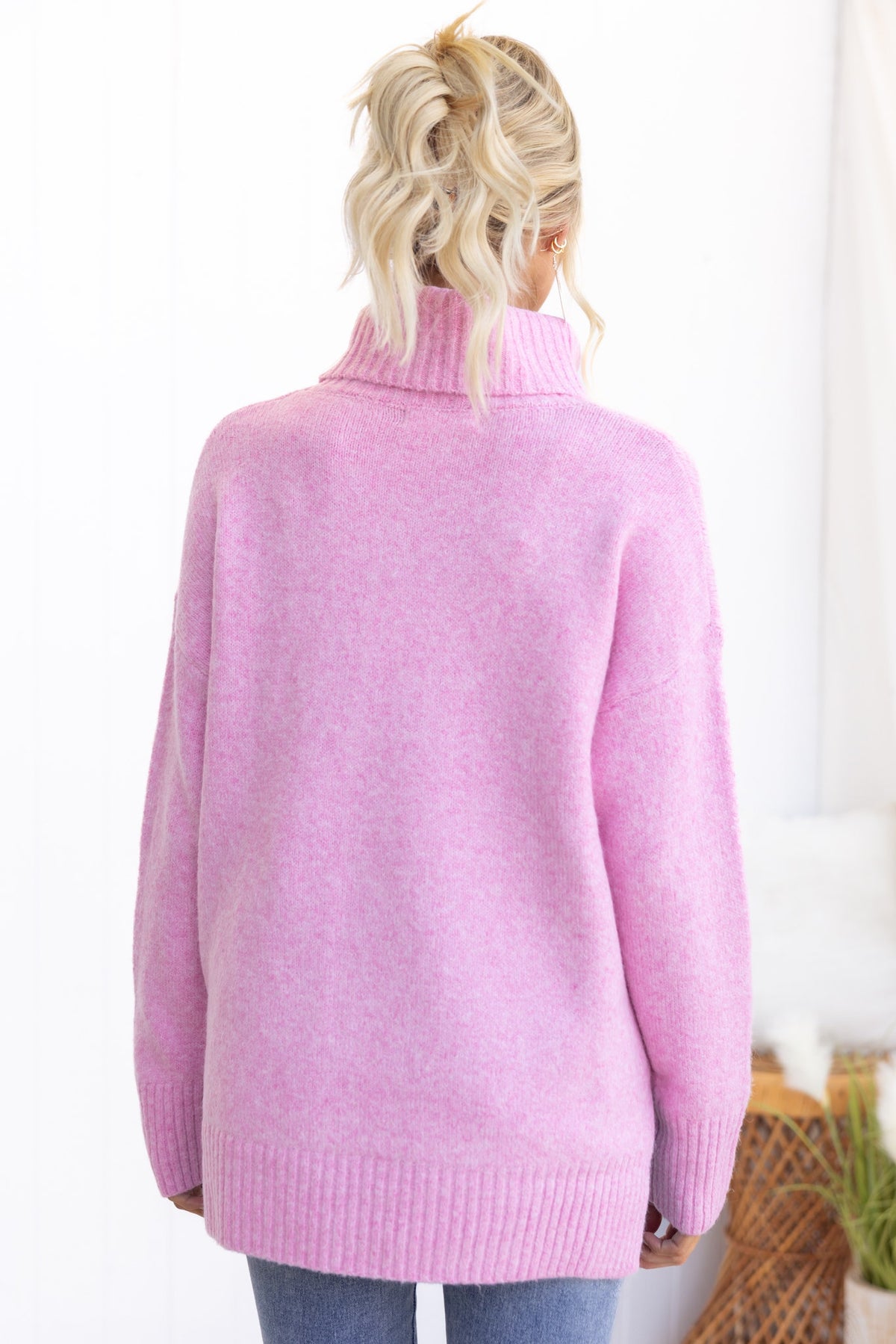 Back view of a relaxed pink Orion Jumper with turtle neckline and ribbed hem, styled casually with jeans.