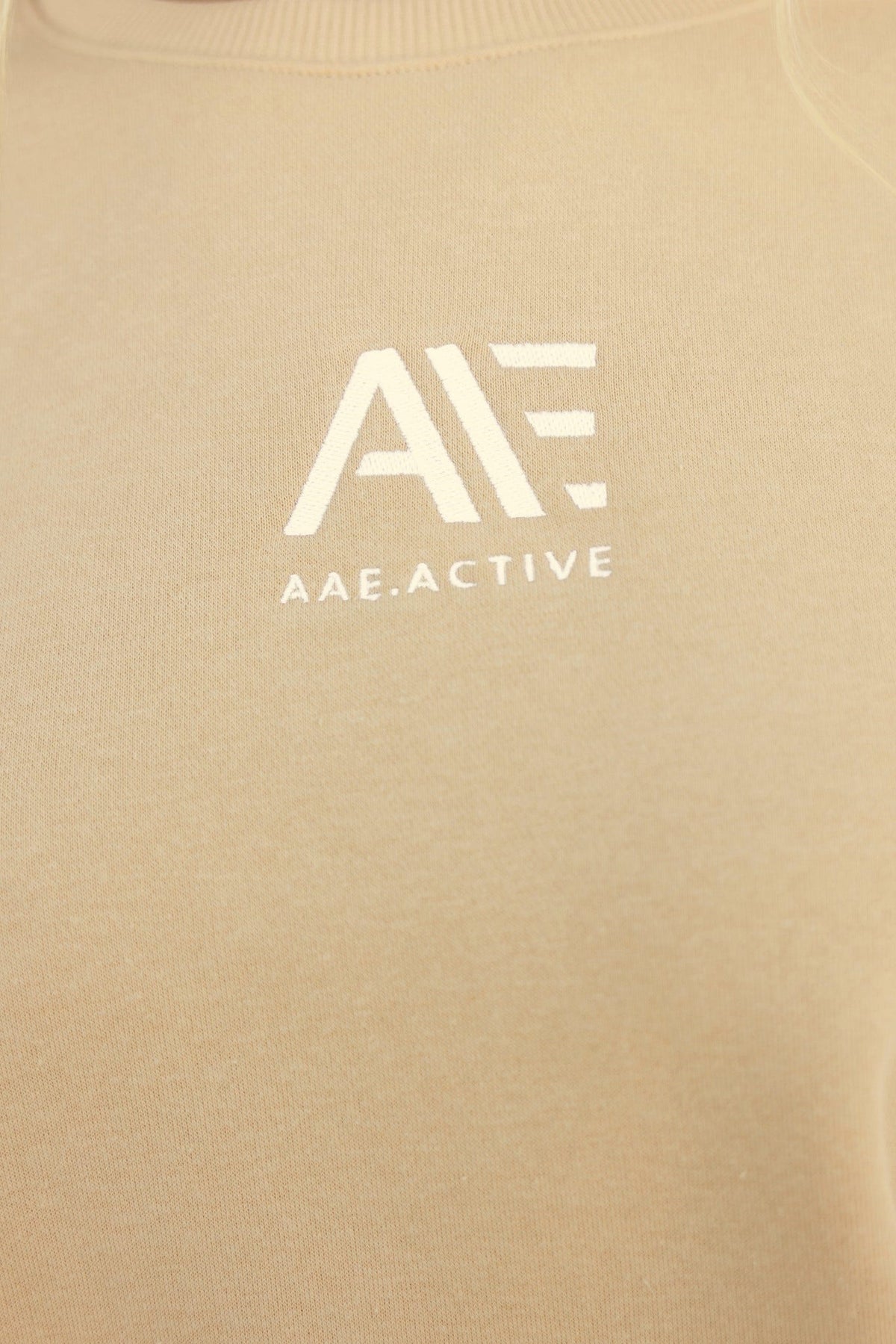 Close-up of AAE Active logo stitched on beige Elana Jumper, showcasing its soft fleece fabric and premium quality.