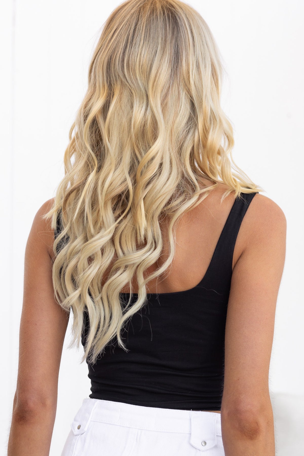 Back view of a woman in a black Snalla Top with gathered bust and wavy blonde hair, showcasing casual style.