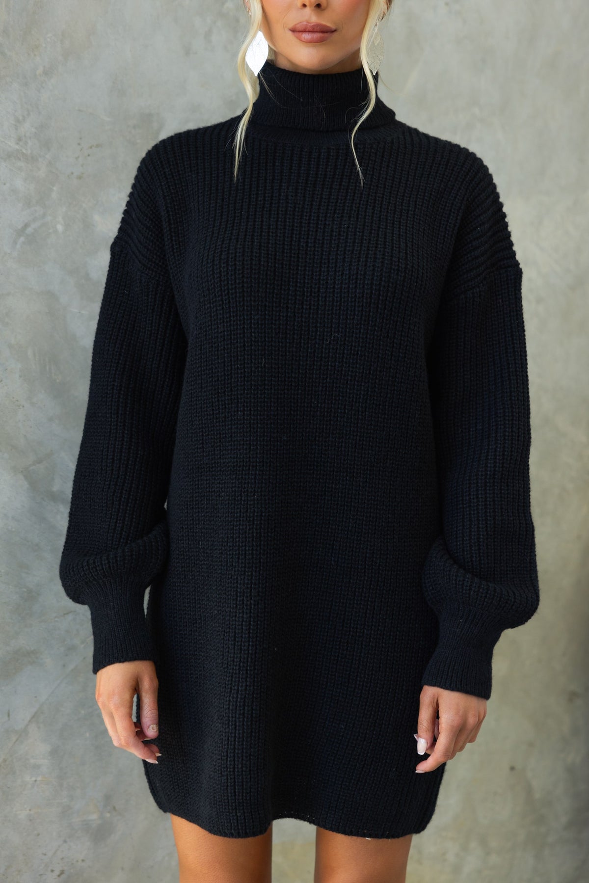 Model wearing Whinnie Dress, a relaxed fit black knit dress with turtle neckline and oversized sleeves.