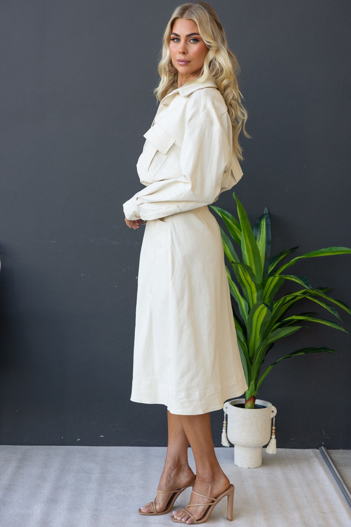 Model wearing a Ronin Denim Midi Dress in cream with button-up front and pockets, styled with heels.