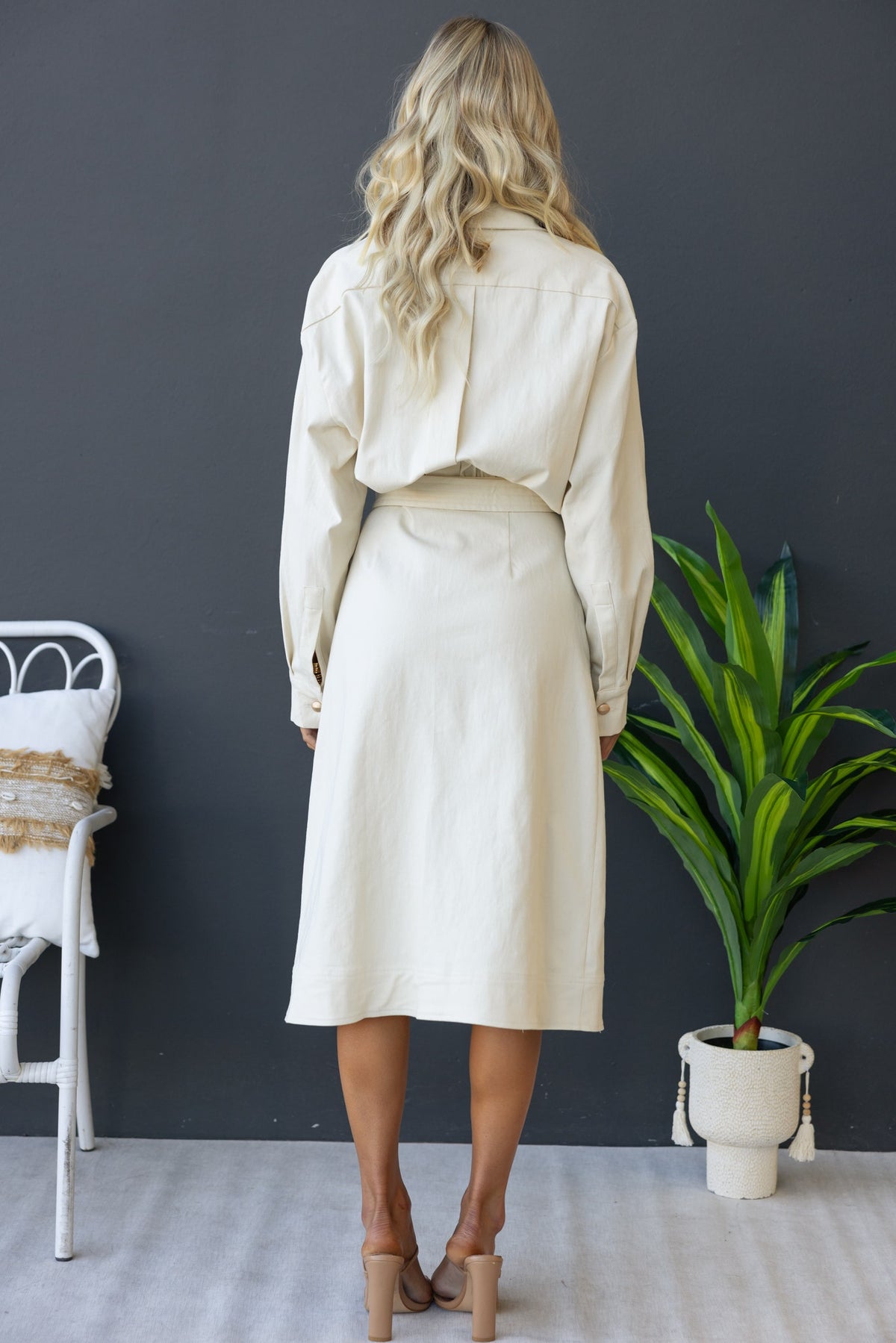 Model wearing a beige denim midi dress, featuring a button-up front and a relaxed fit, viewed from the back.