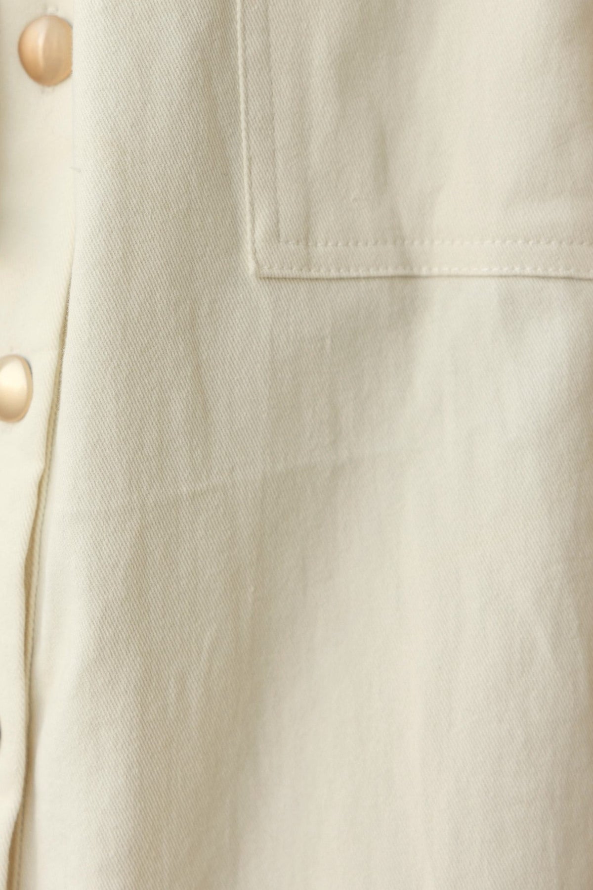 Close-up of beige denim fabric with button details and stitched pocket for the Ronin Denim Midi Dress.