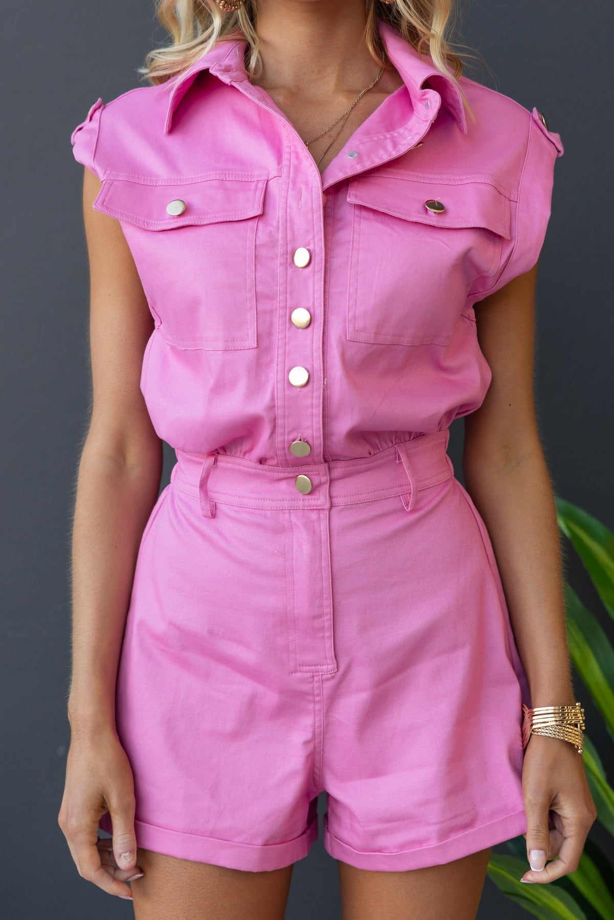 Model wearing a pink denim playsuit with a button-up front and pockets, featuring rolled sleeves and a fitted high waist.