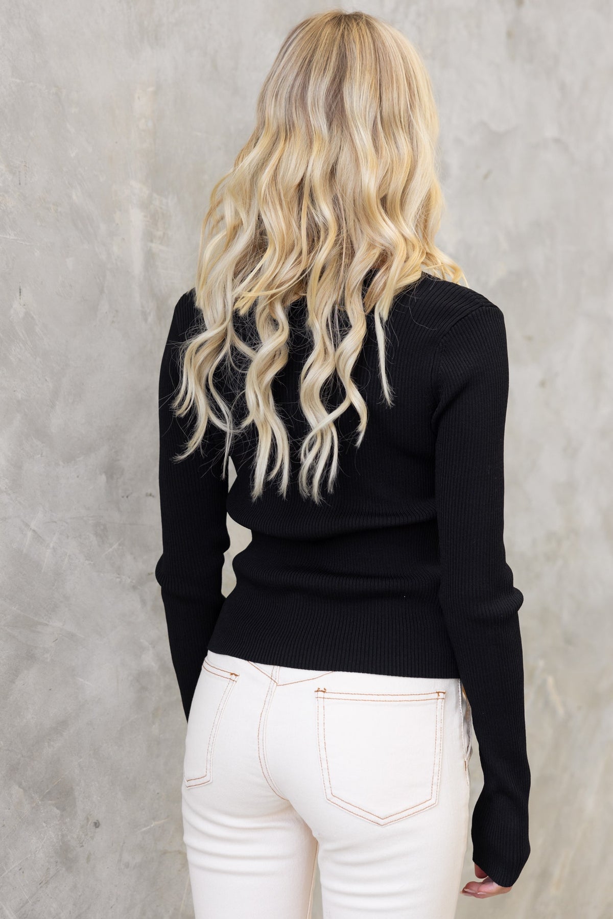 Back view of a woman in a black ribbed top, paired with white jeans, showcasing a stylish outfit.
