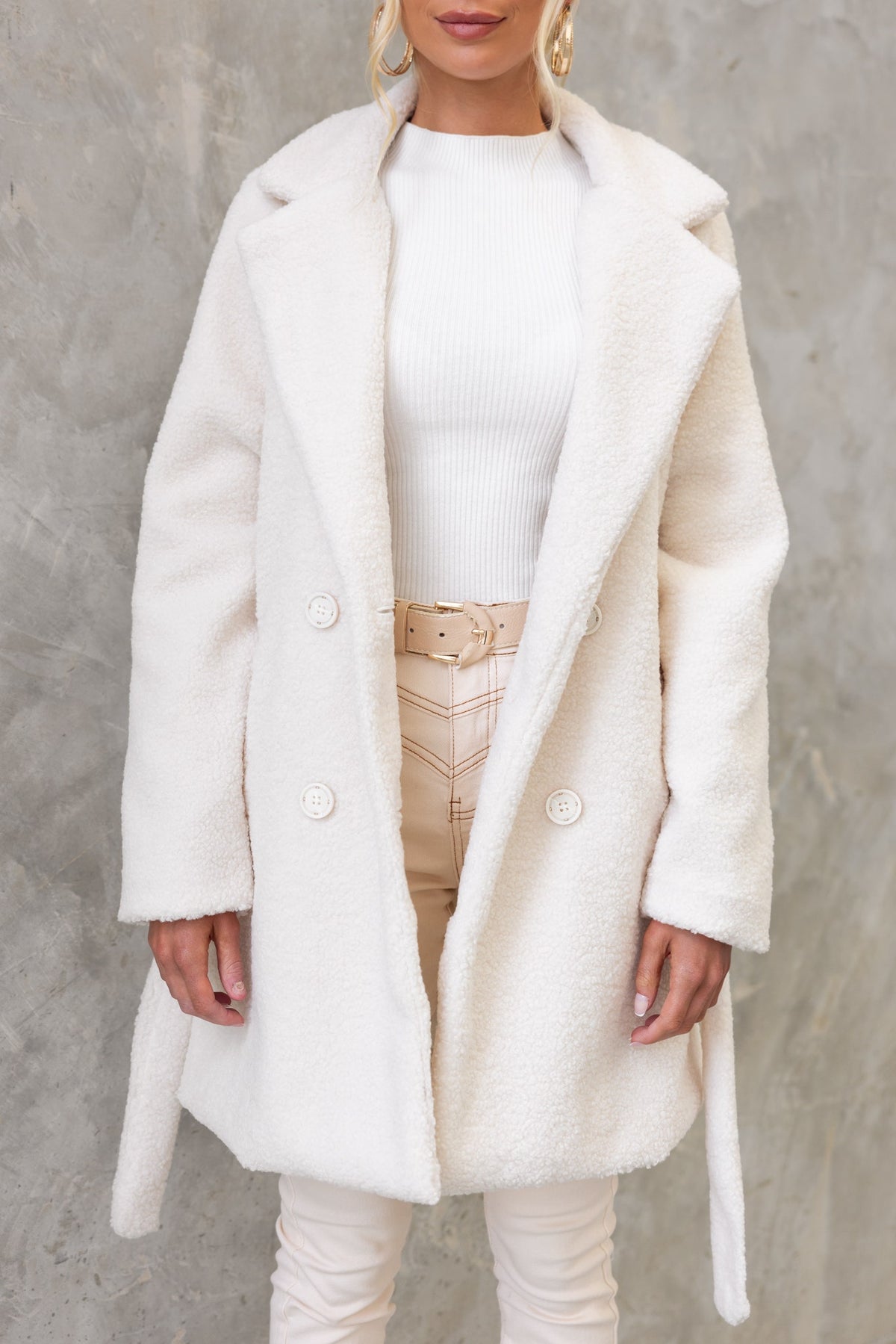 Model wearing a stylish ivory teddy coat with a double-breasted front and a relaxed fit over a white top and beige pants.