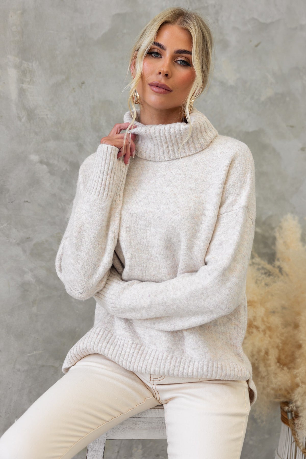 Model wearing an Orion Jumper featuring a turtle neckline and ribbed knit design, styled with beige pants.