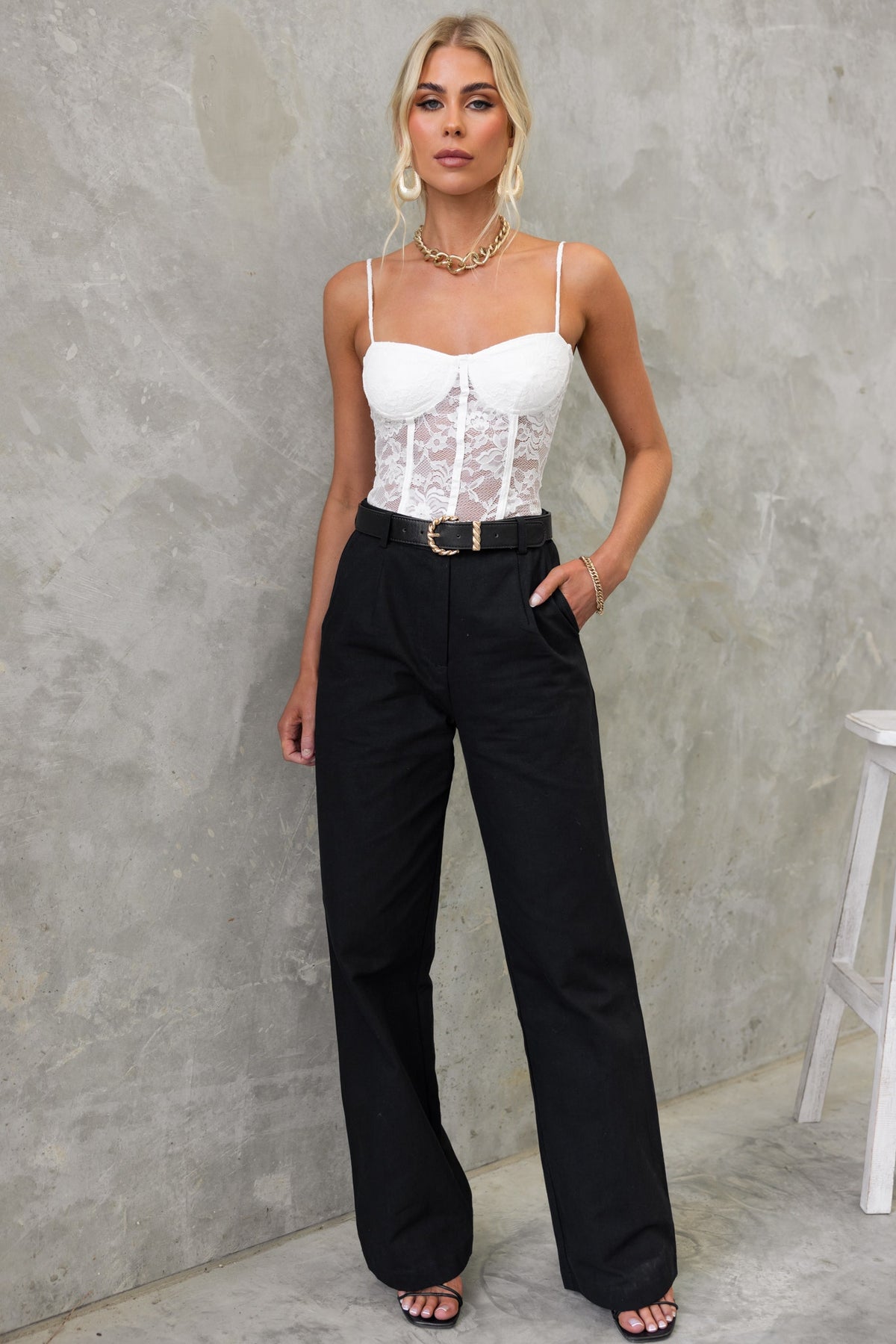 Model wearing Rayden Denim Pants with wide legs and mid-high waist, styled with a white lace bodysuit and fashionable accessories.