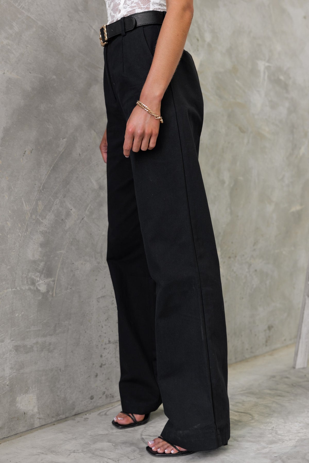Model wearing Rayden Denim Pants, high-waisted black jeans with wide legs, styled with a belt and sandals.