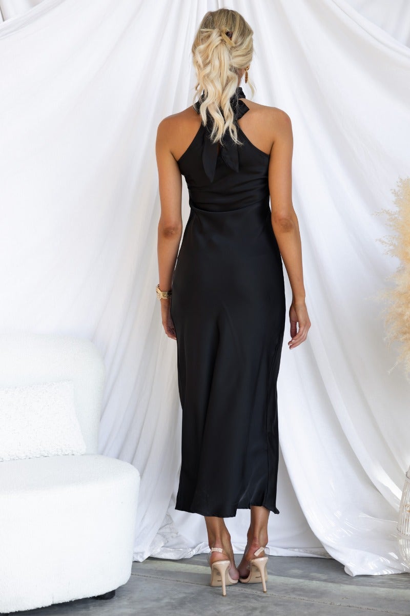 Back view of a woman in a black satin maxi dress with high tie neckline, showcasing elegant silhouette.