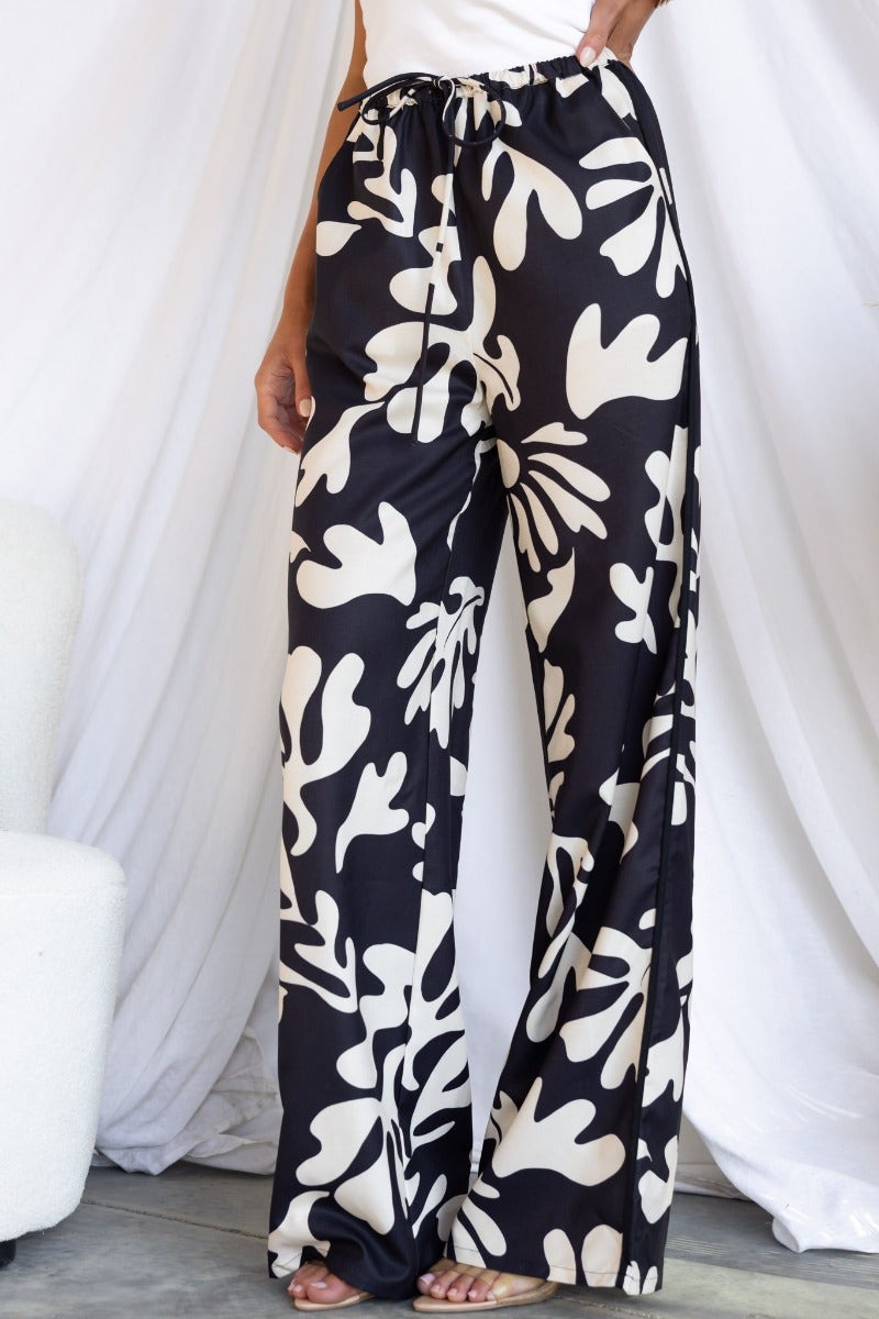 Trendy White Lies Pants featuring a black and white abstract print, elastic waistband with drawstring, and wide-leg fit.