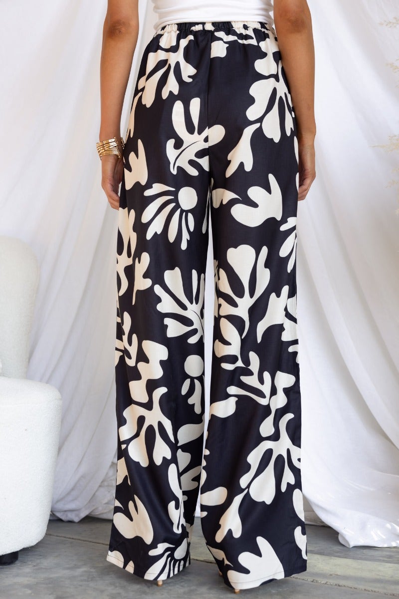 White Lies pants featuring a black and white leaf print, elastic waistband with drawstring, and a relaxed fit.