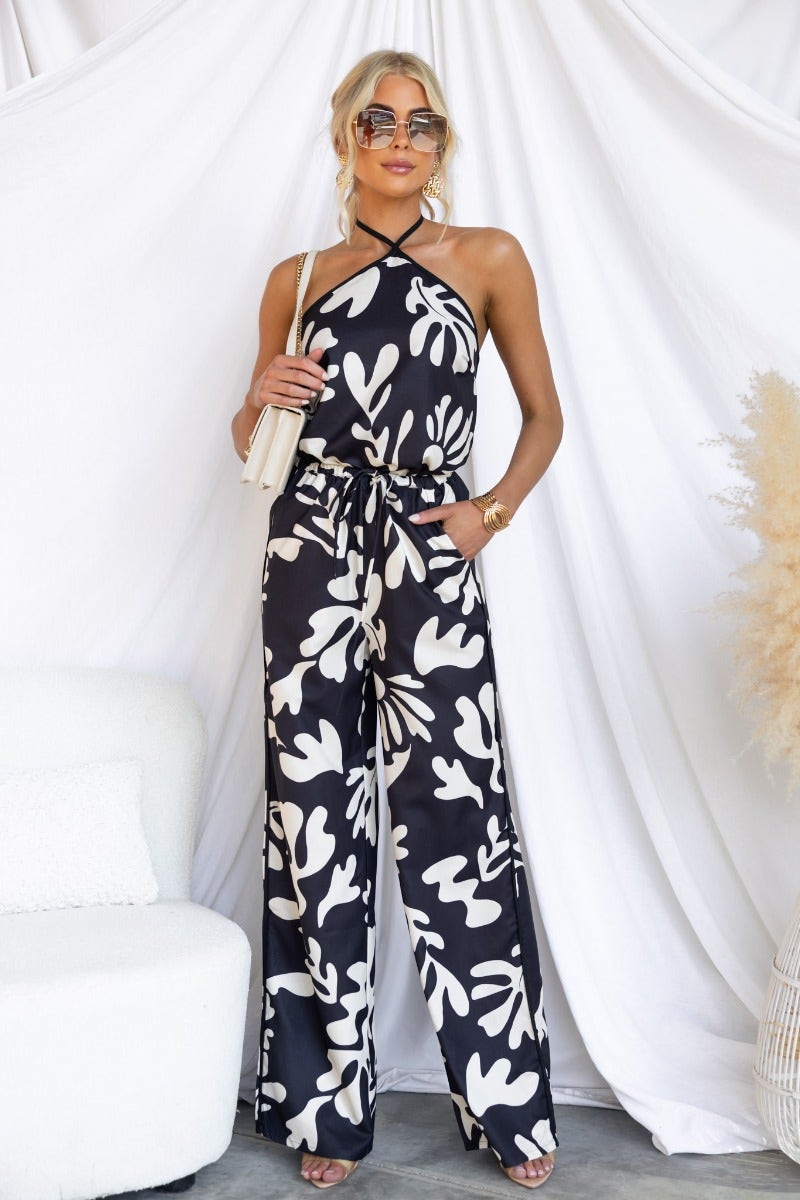 Model in a Black and White floral print top with adjustable tie halter neck, styled with wide-leg pants.