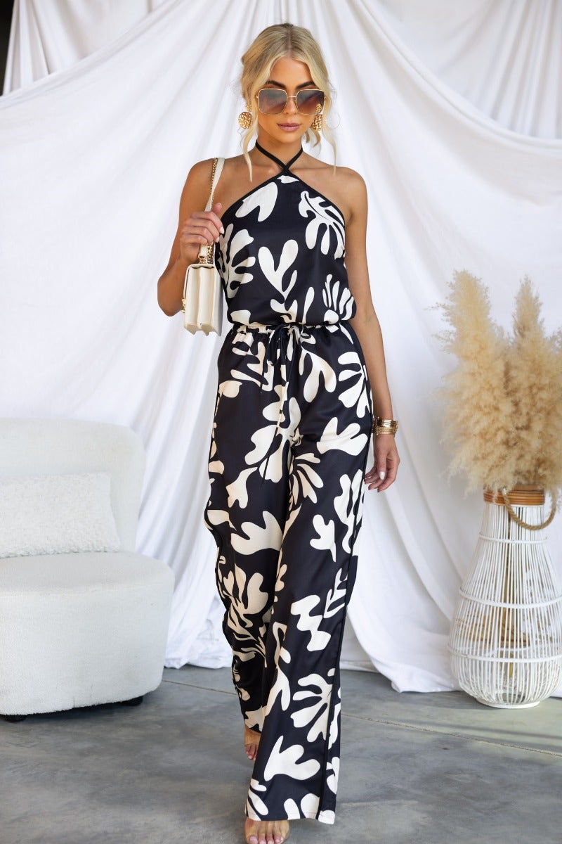 Model wearing White Lies pants with a black and white floral print, styled with accessories and sunglasses.