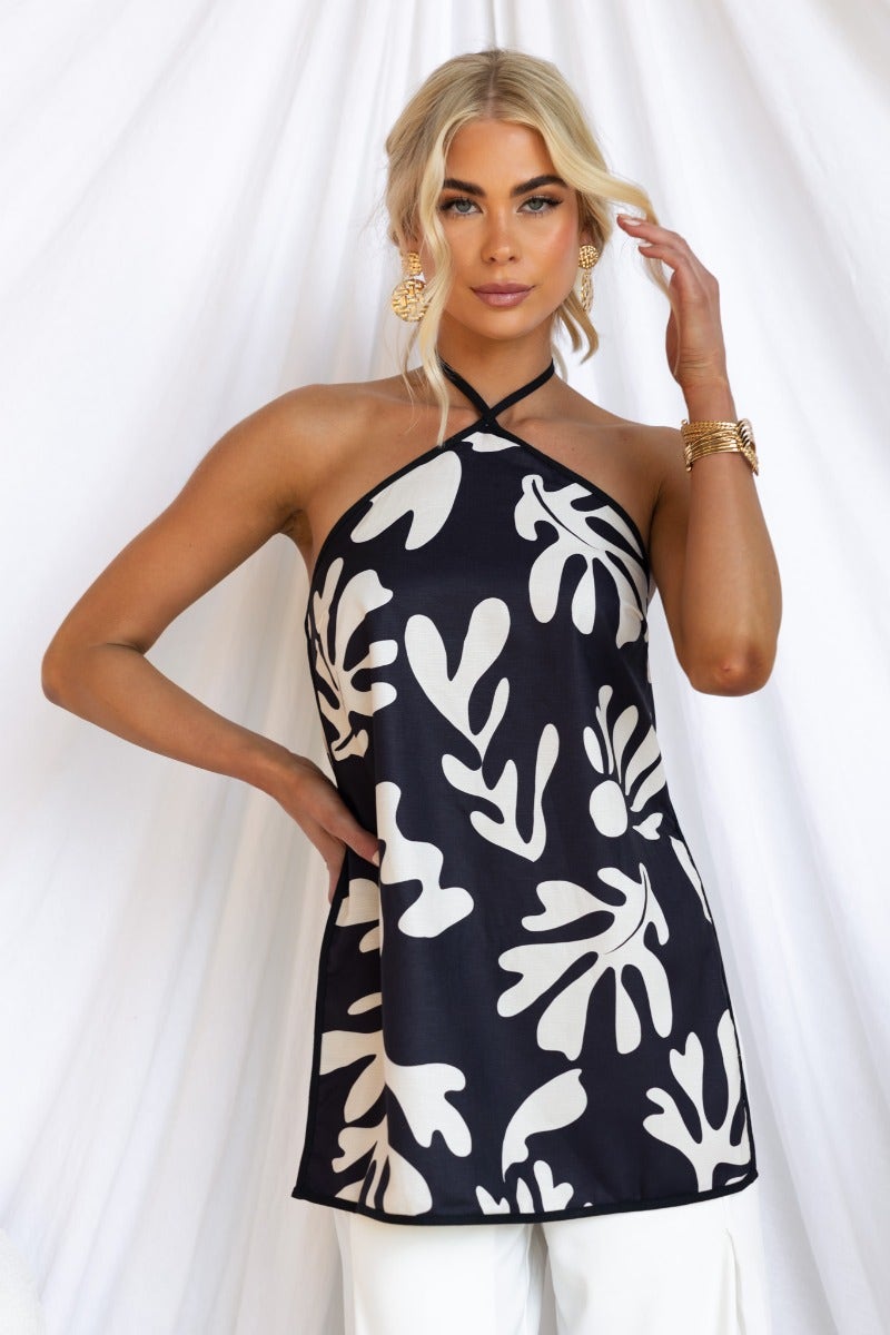 Model wearing a black and cream floral print top with adjustable tie halter neckline and side splits.