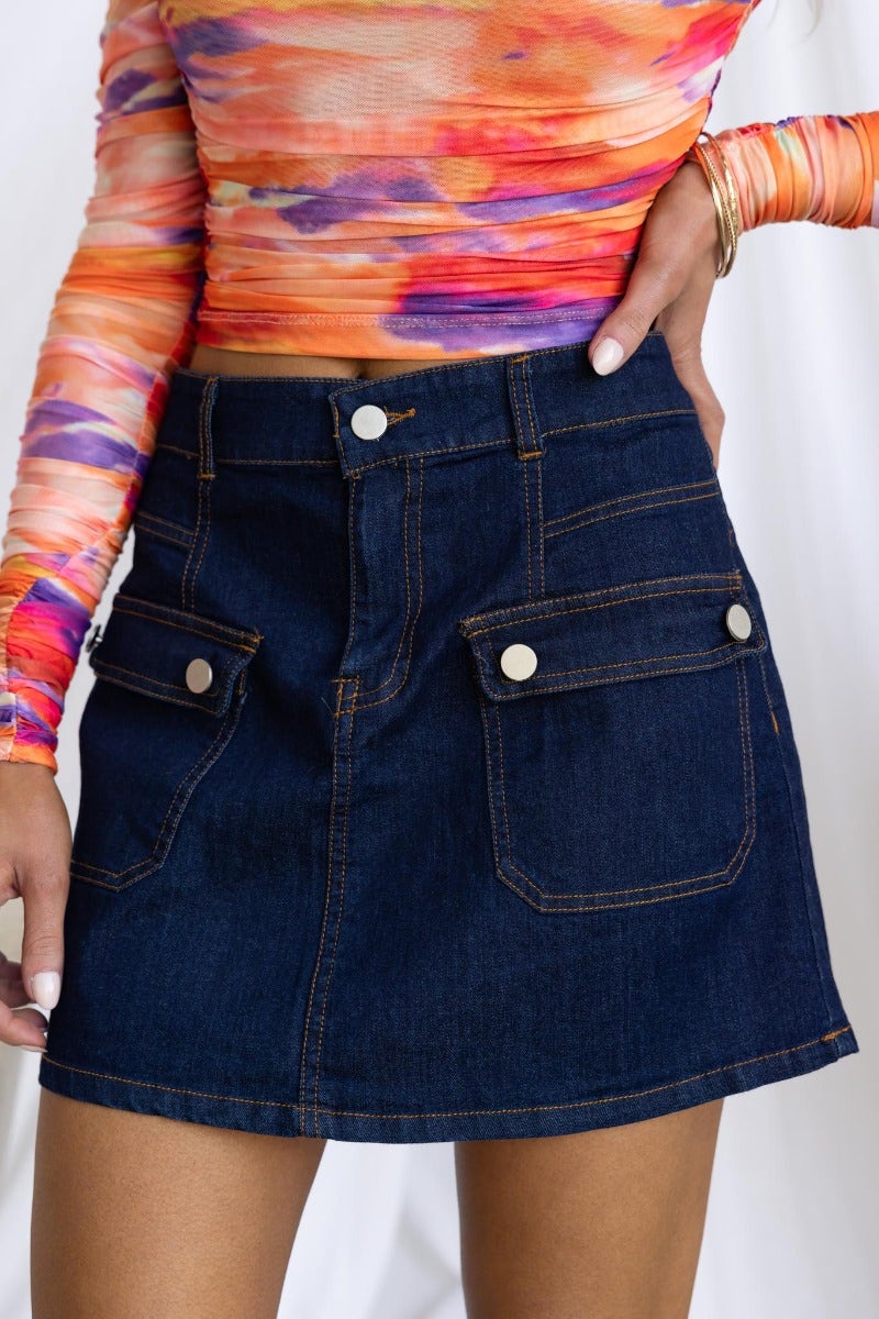 Model wearing a Lewis Denim Skirt featuring a mid-low waist fit and front pockets, styled with a colorful top.