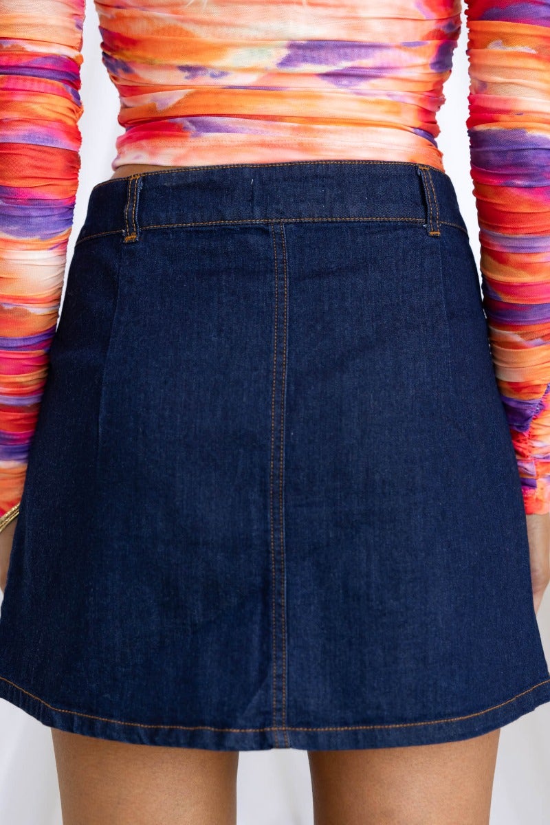 Model showcases the back of a Lewis denim skirt featuring a mid-low waist fit and pockets against a colorful top.