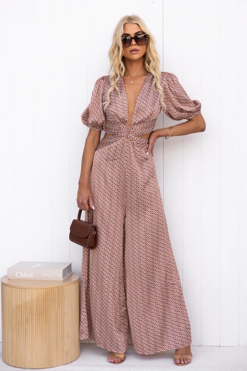 Model wearing a Soho Satin Jumpsuit with V-neckline and cut-out waist, paired with sunglasses and a small handbag.